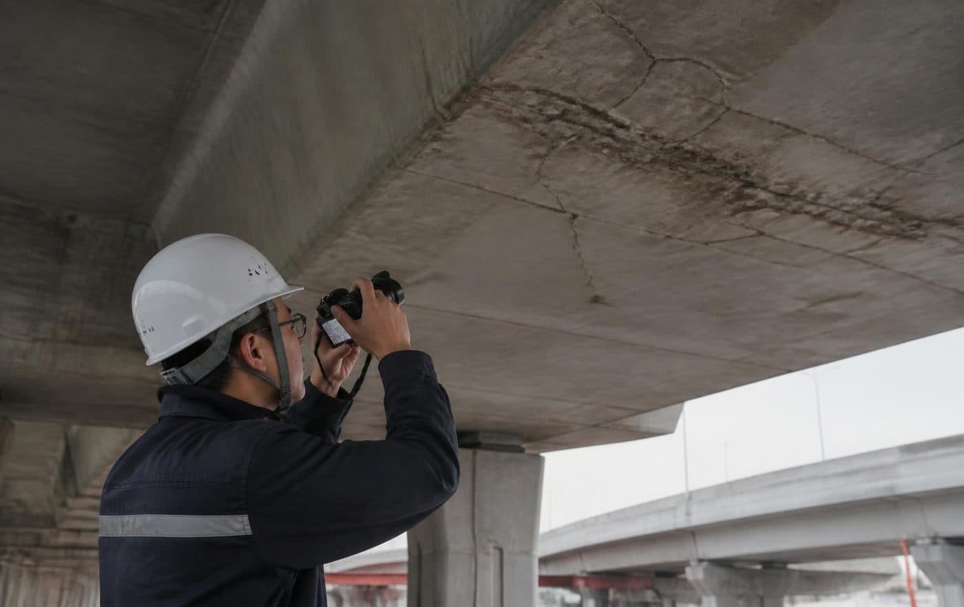 Engenheiro registrando fissuras na face inferior de um viaduto durante vistoria técnica